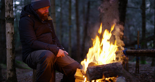 Man uses compass and smart phone by campfire in the forest