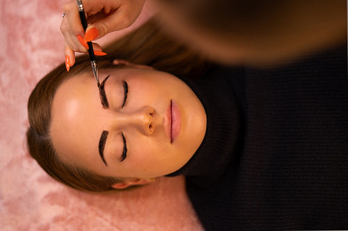 Cosmetologist Applying Dye On Female Customer's Eyebrow