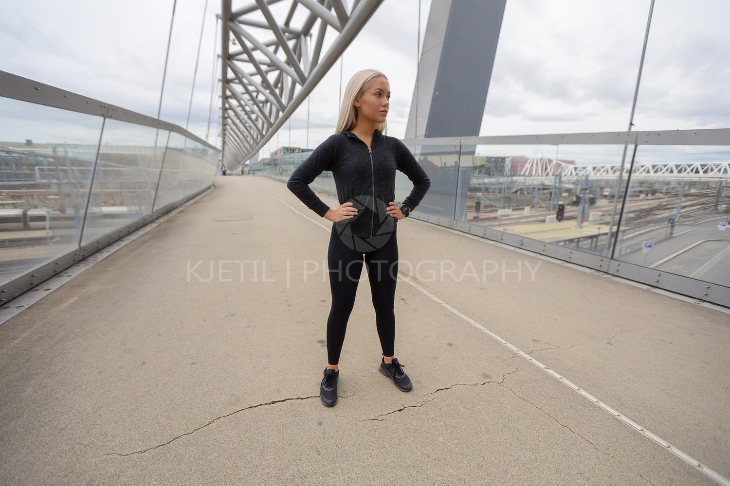 Blonde Female Beauty in Black Workout Wear Standing At Modern Bridge In City