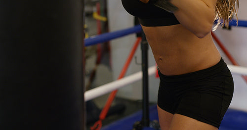 Focused female boxer knocks punching bag in boxing club