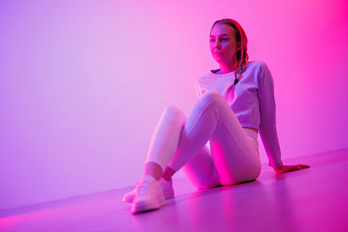 Thoughtful female sitting against neon pink background