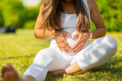 Close-up of pregnant woman sitting outdoor making hand heart gesture on belly