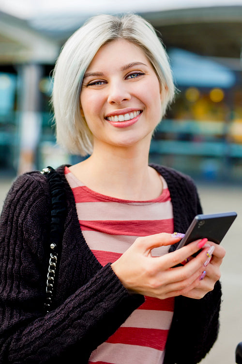 Woman Smiling While Using Smart Phone Outside Train Station