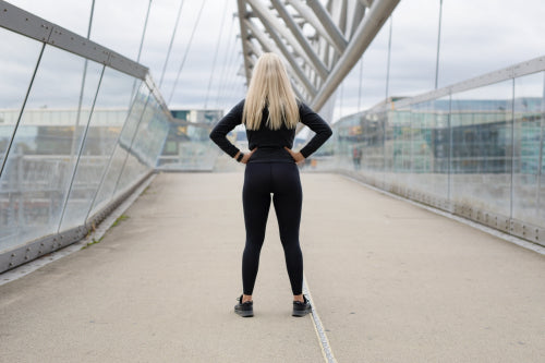 Back of fit blonde woman runner standing on bridge in modern looking city