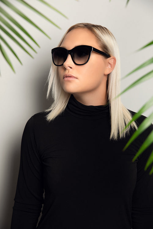 Profile of beautiful woman with sunglasses hiding behind tropical palm leaves