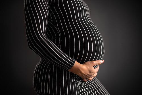 Elegant Pregnant Woman in Striped Dress Holding Her Belly