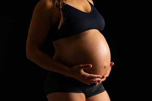 Pregnant Woman Embracing Her Belly on Black Background