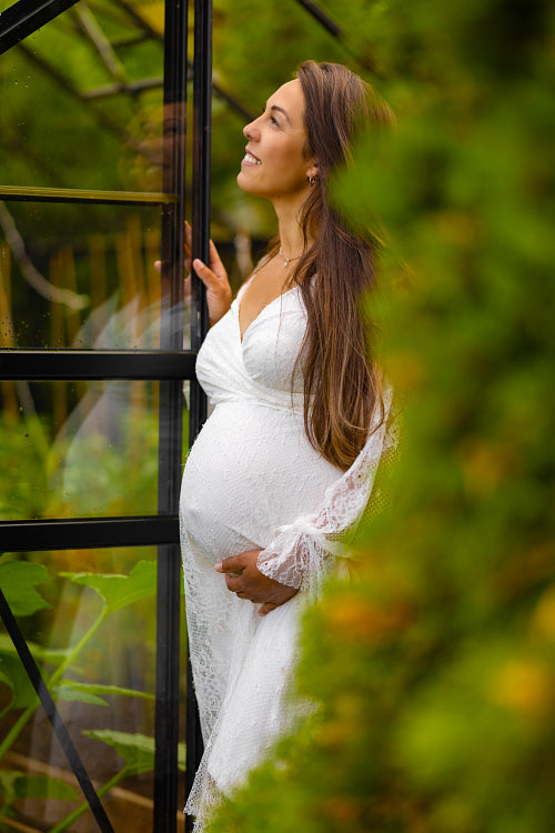 Serene Pregnant Woman Embracing Her Belly in a Greenhouse