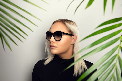 Beautiful woman with sunglasses hiding behind tropical palm leaves