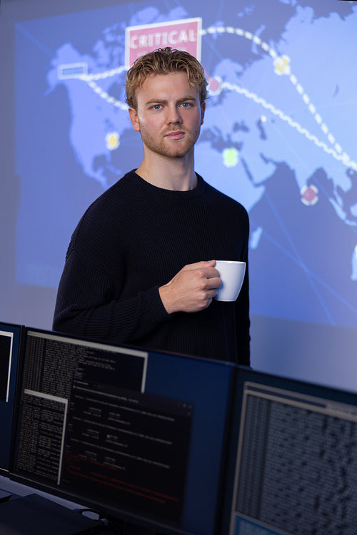 Confident male Cybersecurity Analyst with coffee cup in large Cyber Security Operation Center SOC handling Threats