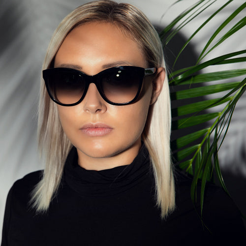 Close-up of woman with sunglasses hiding behind tropical palm leaves
