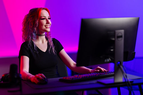 Professional gamer smiling while playing a PC game in a vibrant room with neon lighting