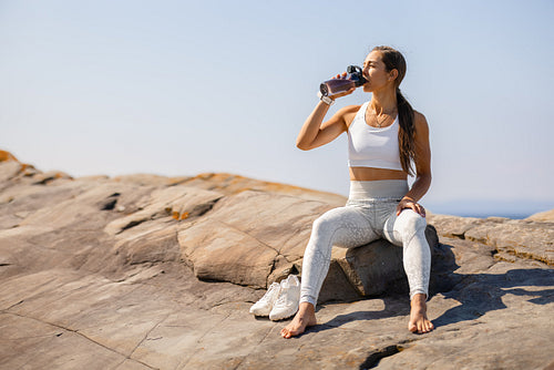 Young Woman Drinking Water After Outdoor Workout on Rocky Terrain