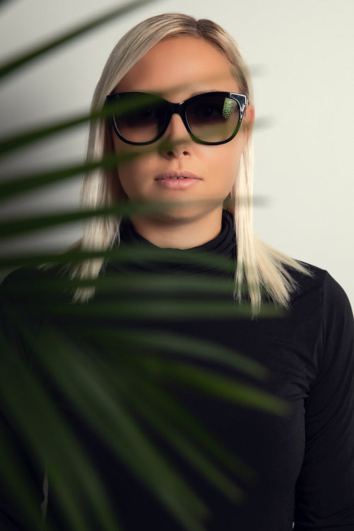 Beautiful woman with sunglasses hiding behind tropical palm leaves