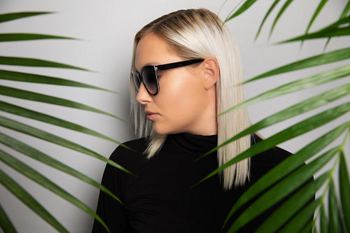 Profile of beautiful woman with sunglasses hiding behind tropical palm leaves
