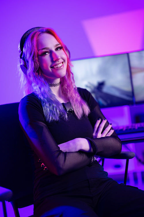 Portrait of a smiling e-sport gamer girl sitting in front of her computer in her colorful gaming room