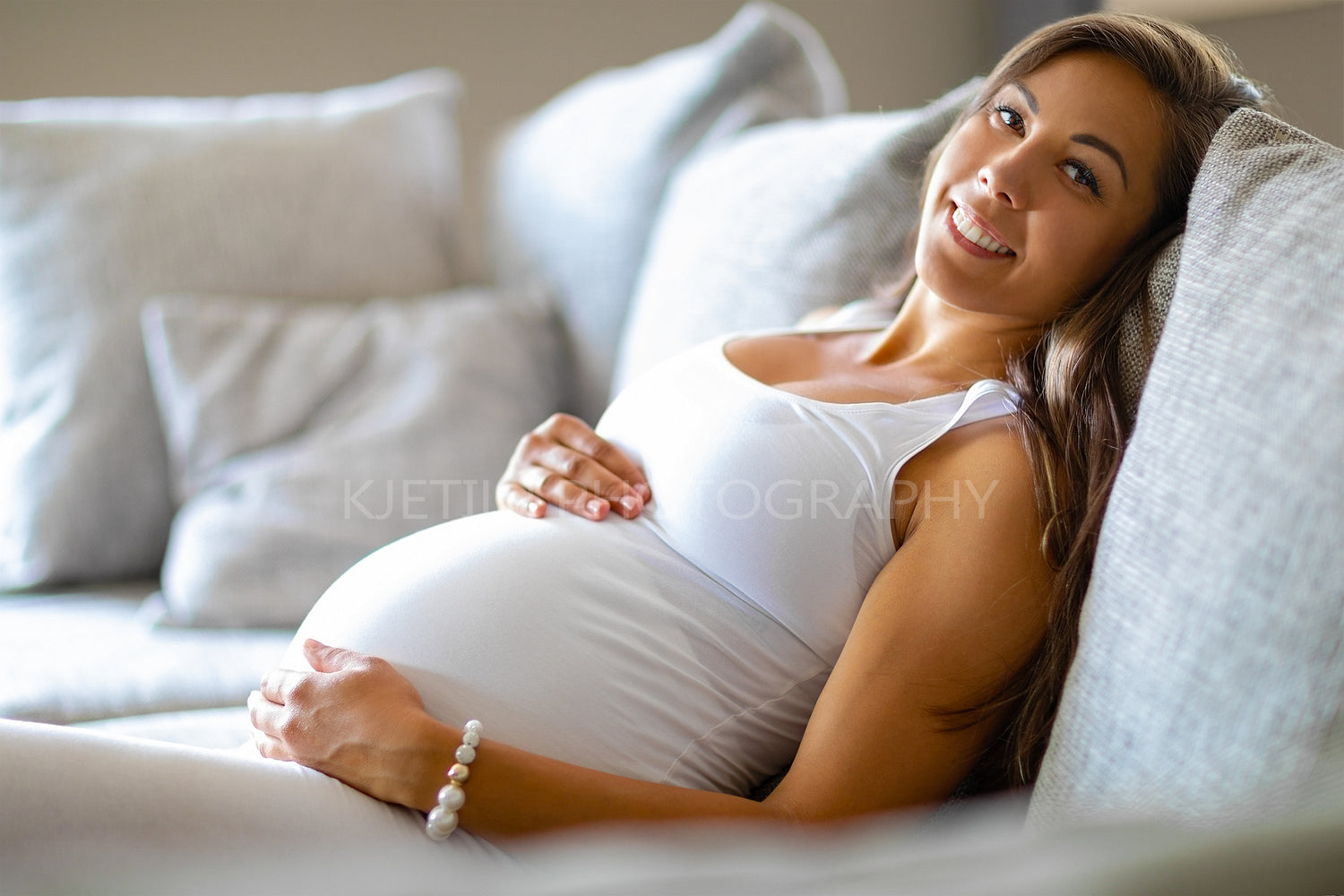 Smiling pregnant woman lying on the sofa touching her belly