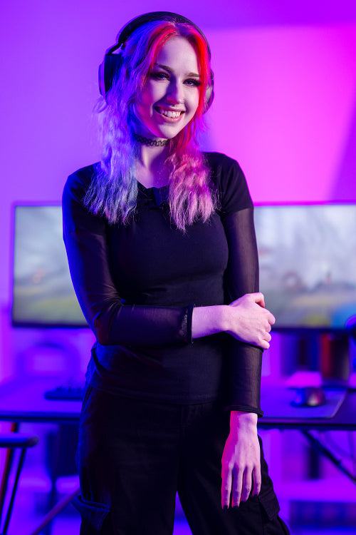 Portrait of a smiling e-sport gamer girl in front of her computer in her colorful gaming room