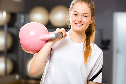 Smiling woman in workout outfit holds kettlebell at fitness gym