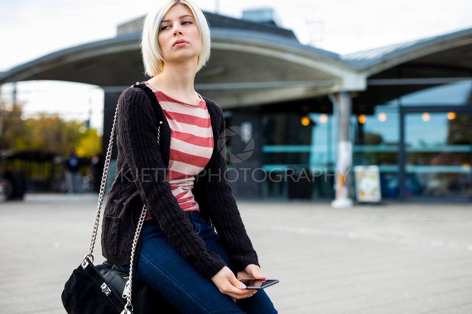 Bored Woman With Mobile Phone Sitting On Luggage Outside Station
