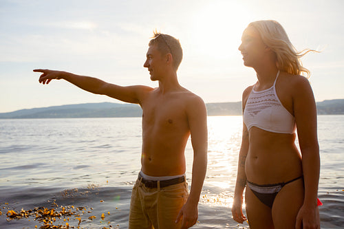 Smiling Young Man Pointing To Girlfriend Standing At Beach