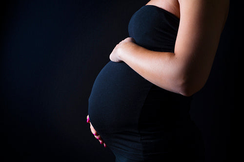 Pregnant woman stands with her hands at the belly