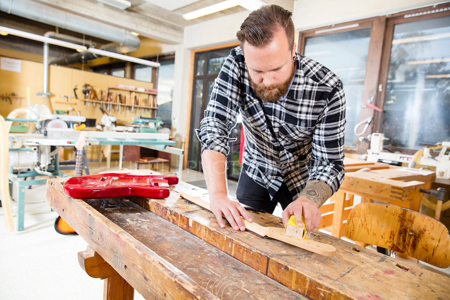 Carpenter sanding a wooden guitar neck in workshop