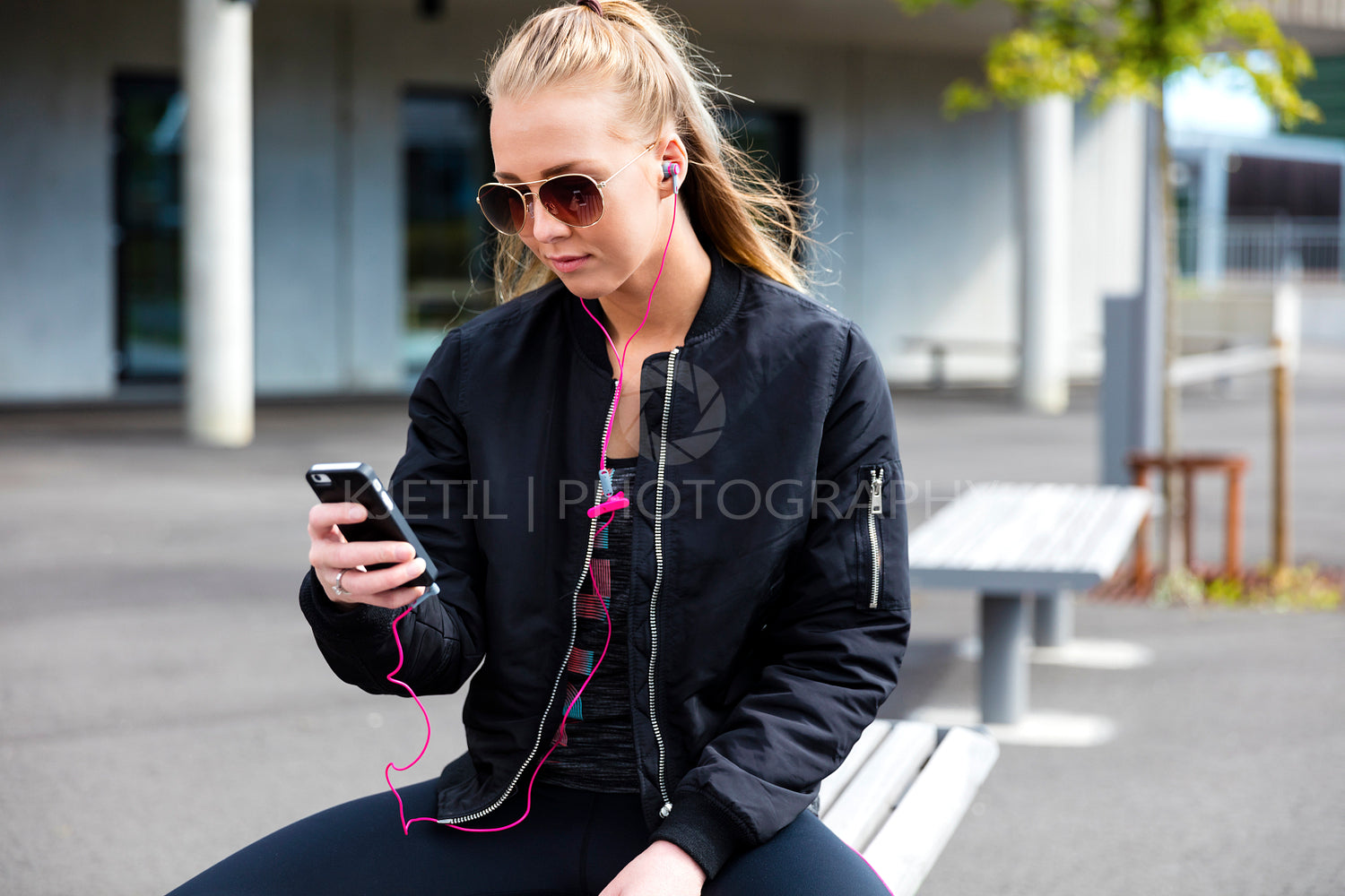 Blonde woman with sunglasses sits outdoor and uses phone