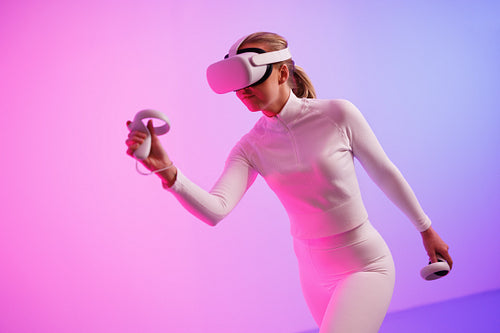 Female in VR glasses workout by illuminated neon room