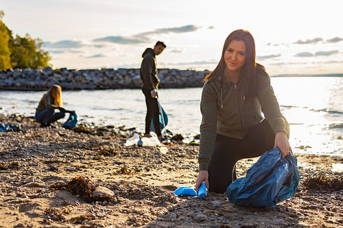 Smiling young woman cleaning beach with a team of volunteers during sunset