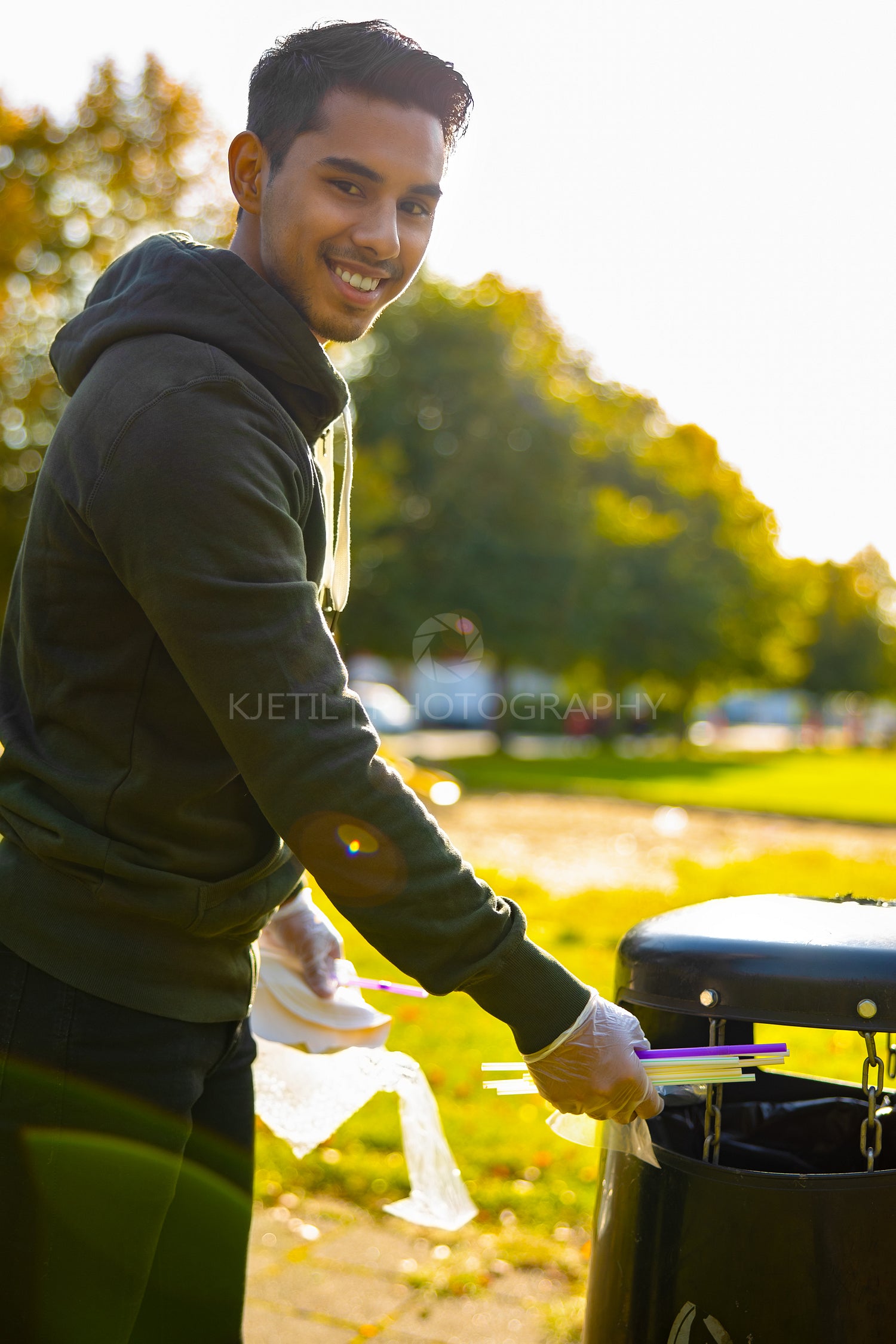 Smiling young man putting straws in garbage bin at park