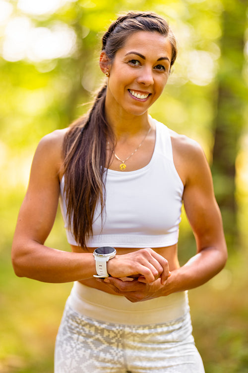 Smiling Athletic Woman In Sportswear Using smart watch device in the forest
