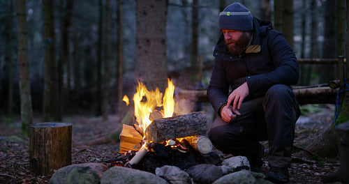 Man warms himself at camp fire in the woods