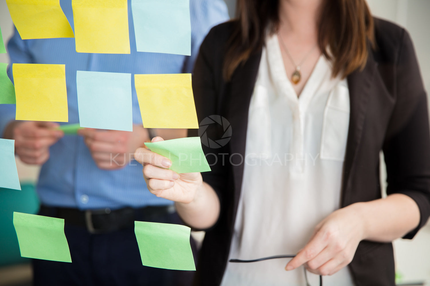 Midsection Of Businesswoman Sticking Note On Glass By Executive