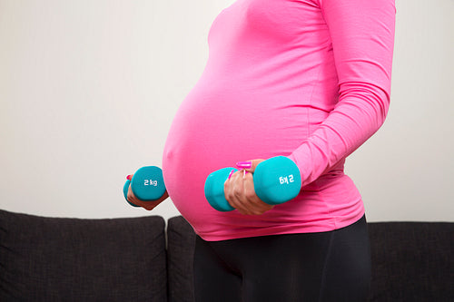 Pregnant young woman exercising with training weights indoor