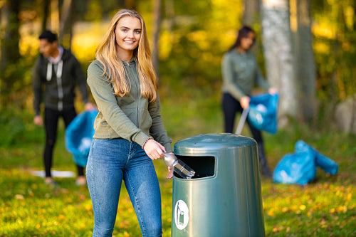 Smiling young woman putting bottle in garbage bin