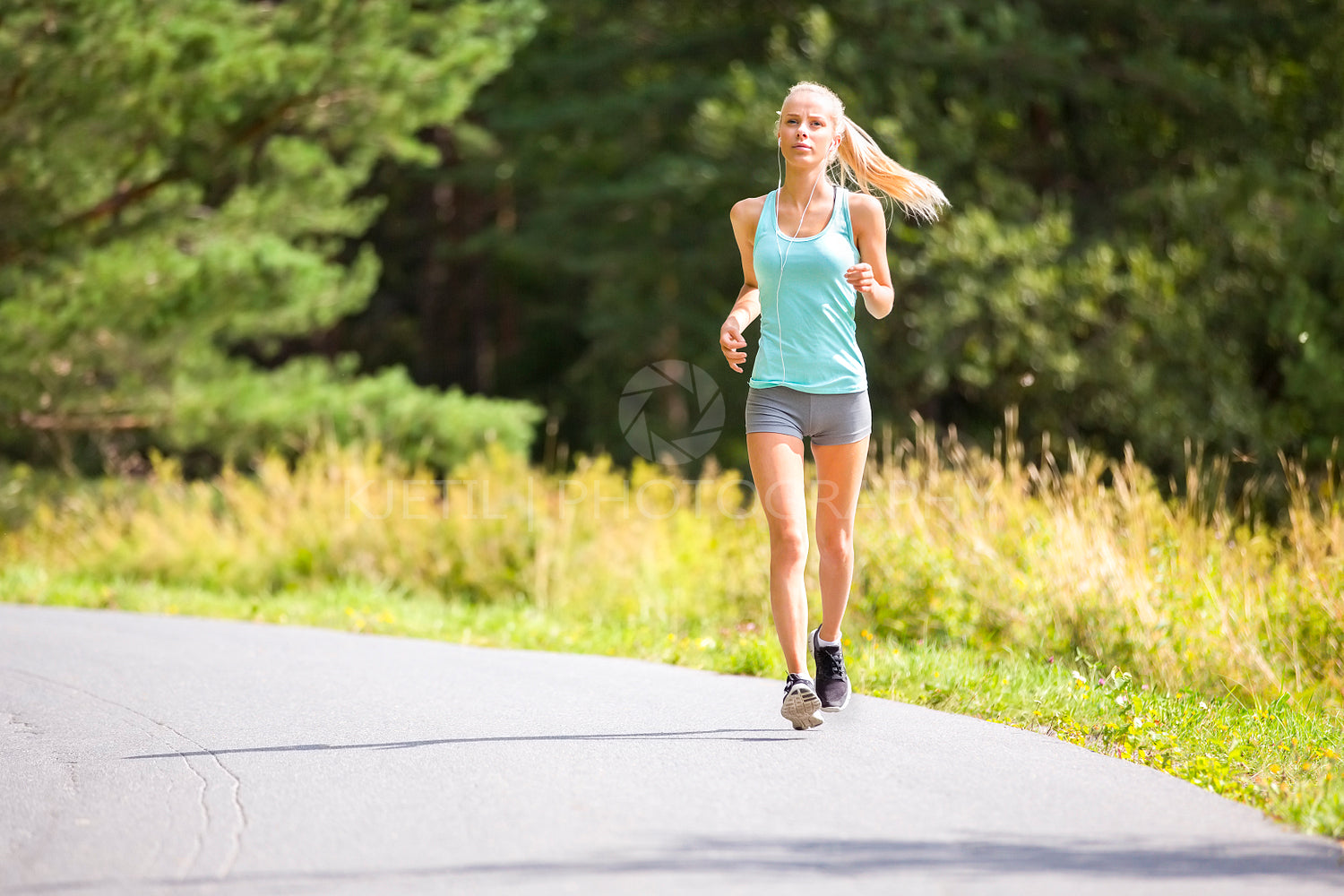 Slim young woman running on a road in the forest