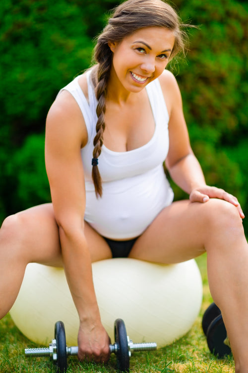 Smiling Pregnant Woman Lifting Dumbbells While Sitting On Yoga Ball