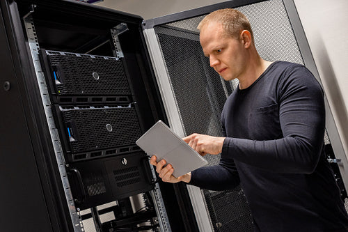 IT Engineer Holding Digital Tablet Analyzing Servers in Datacenter