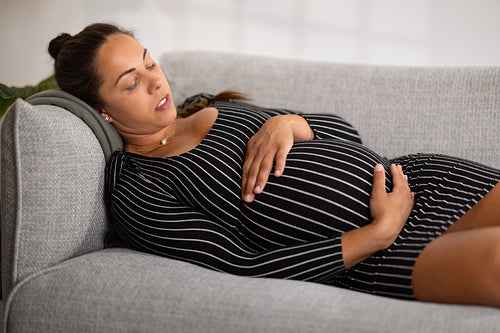 Exhausted and Tired Pregnant Woman in Striped Dress lying in a sofa