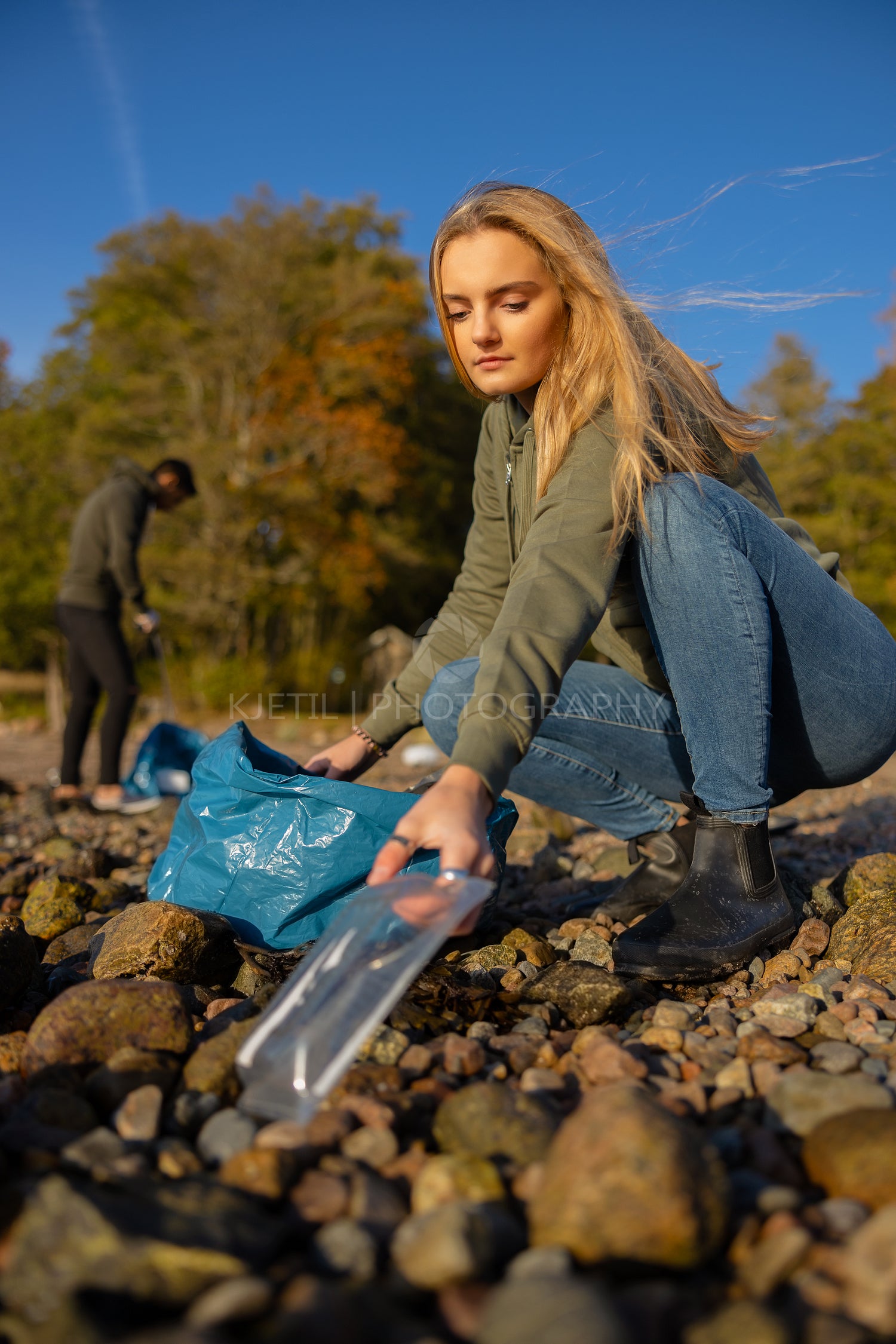 Serious young woman picking up plastic at rocky beach