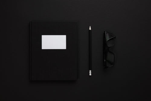 Top view of low key black office desk with notebook and glasses