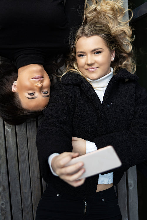 Smiling Friends Lying On Bench Together and Taking Selfie in City