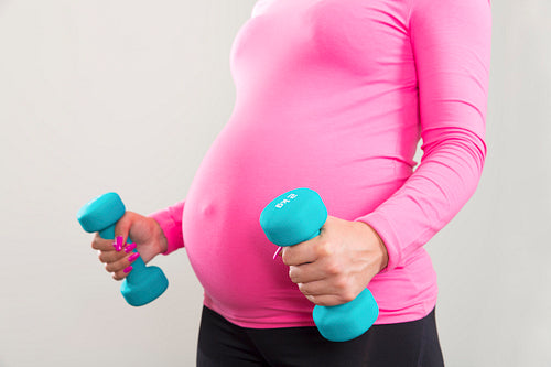 Pregnant woman exercising with training weights indoor