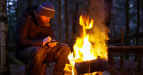Man uses compass and smart phone by camp fire