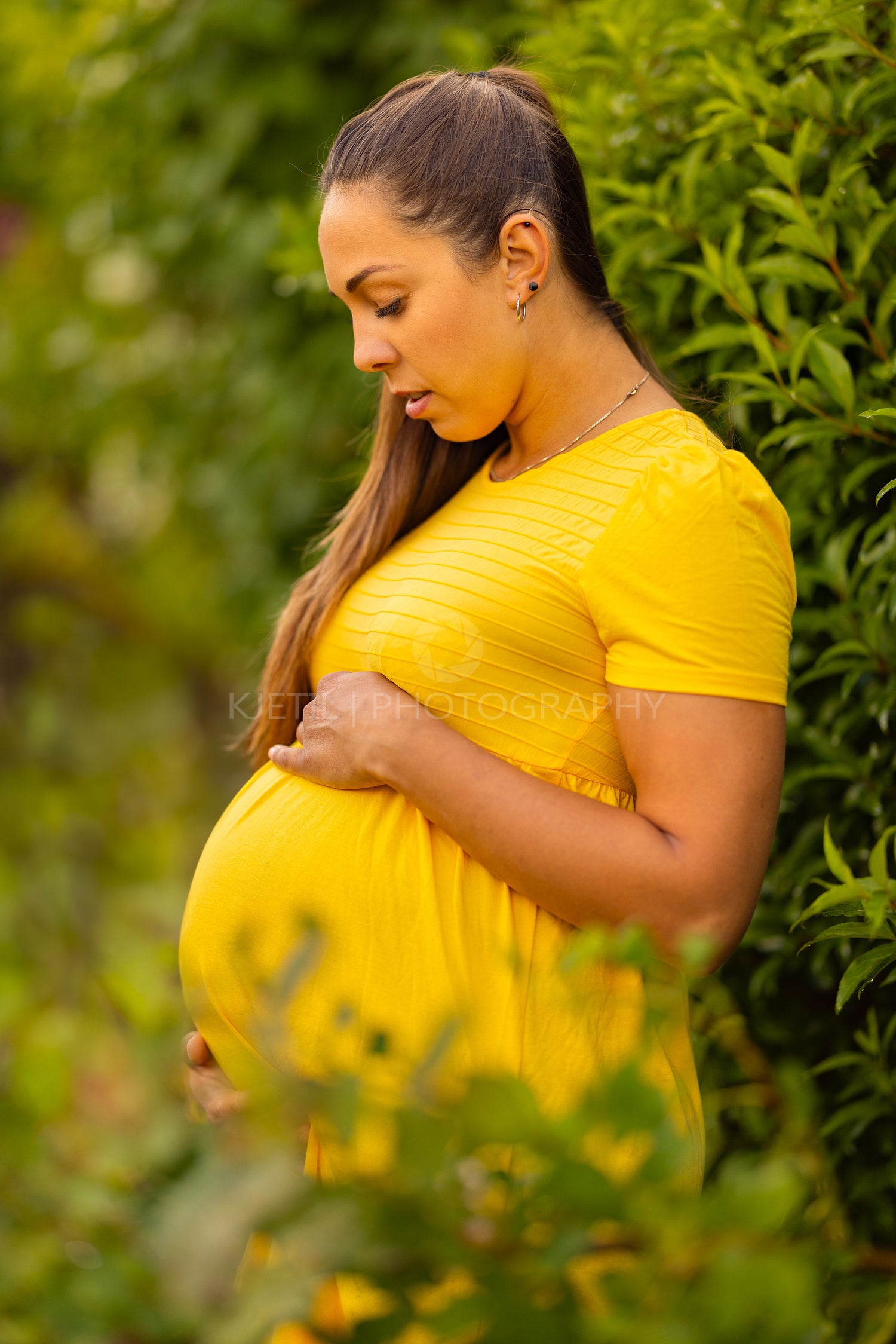 Expecting mother in sunny garden wearing yellow dress