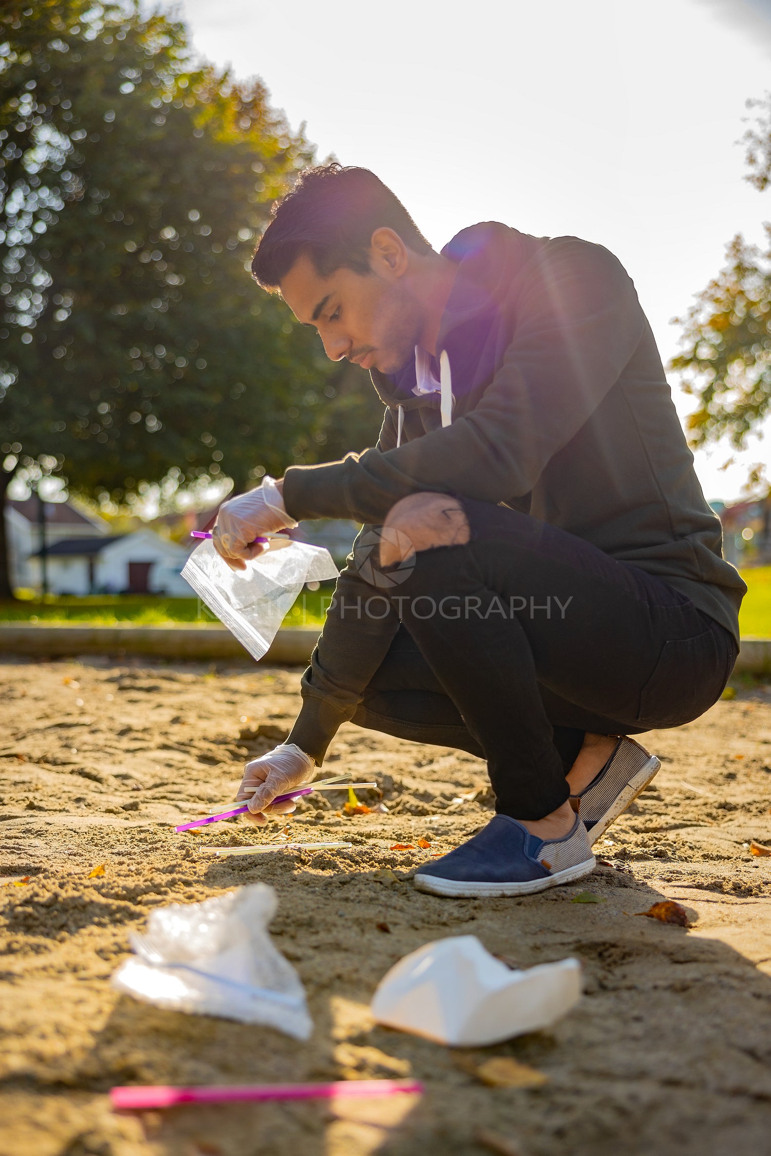 Back lit of male volunteer cleaning garbage on sand at park