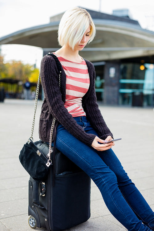 Young Woman Using Mobile Phone While Sitting On Luggage