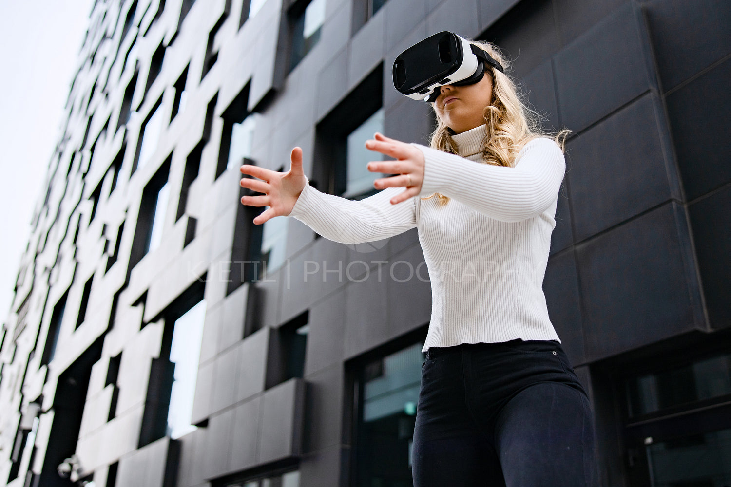 Woman Wearing VR Glasses In Front Of Urban Looking City Building