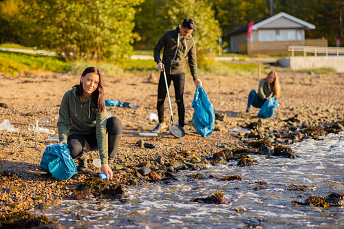 Young woman in a team picking up garbage in bag at beach